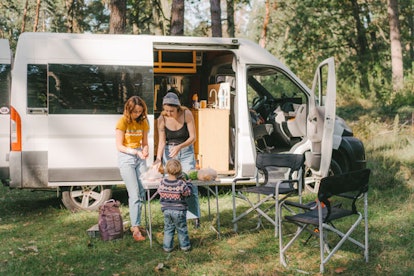 Women and little boy cooking burger on grill in forest