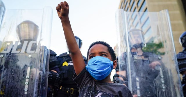 A young boy raises his fist for a photo by a family friend during a demonstration on May 31, 2020 in...