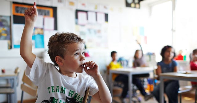 Cute boy with raised hand in classroom