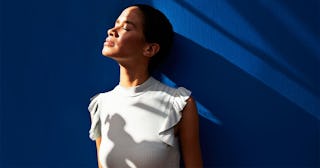 Thoughtful woman standing against blue wall