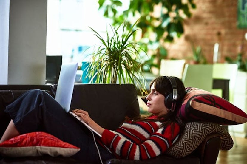 woman at home on sofa using laptop wearing headphones