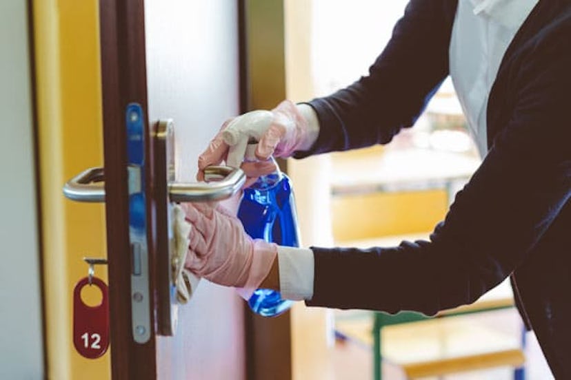 The teacher wipes the door handle in the classroom before students return to school after the corono...