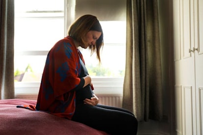 Lone pregnant woman sitting on the bed looking and hugging the belly