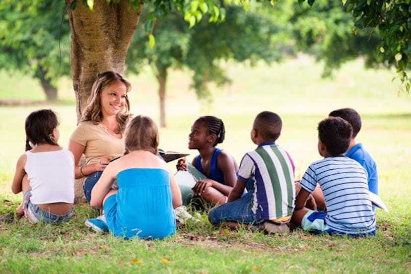 Sitting female teacher surrounded by school-aged children