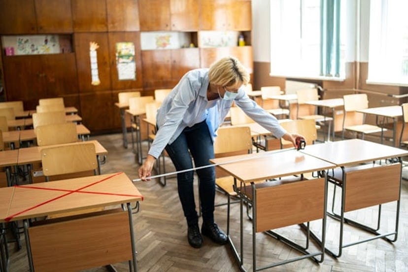 Teacher measuring and marking places in the classroom for returning of students after the coronaviru...