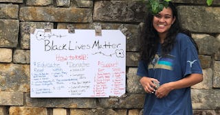 A teenage girl standing next to her Black Liver Matter sign attached to a stone wall