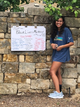 A teenage girl standing next to her Black Liver Matter sign attached to a stone wall