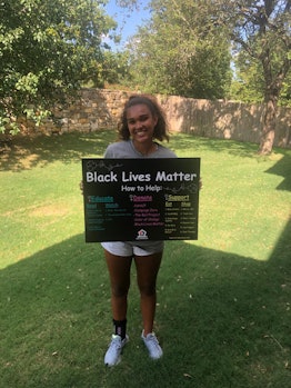 A teenage girl standing in a garden and smiling while holding a BLM poster in her hands