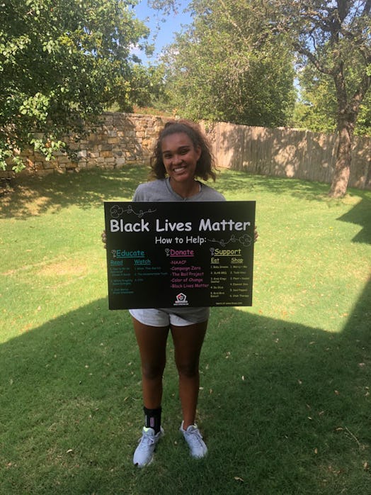A teenage girl standing in a garden and smiling while holding a BLM poster in her hands