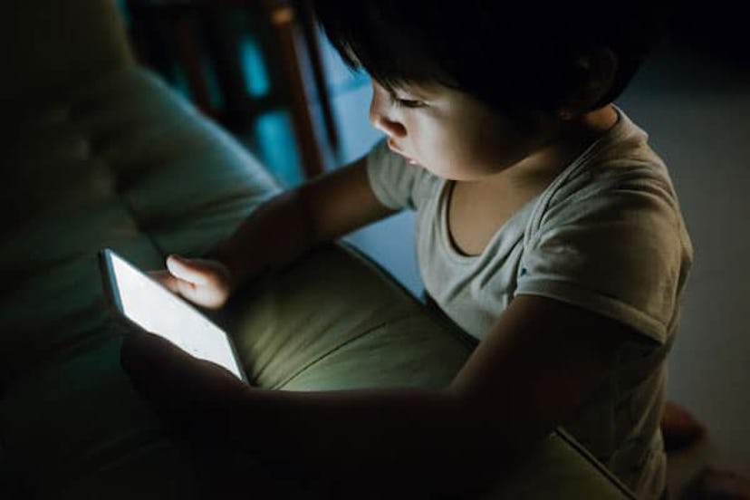 Little kid concentrated on playing with smartphone in the dark