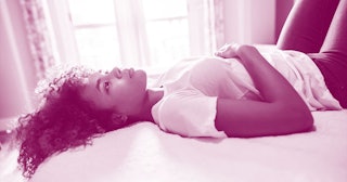 Thoughtful young woman with curly hair lying in bed at home