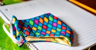 Face mask resting on top of back to school supplies of paper, pencil and a clip board