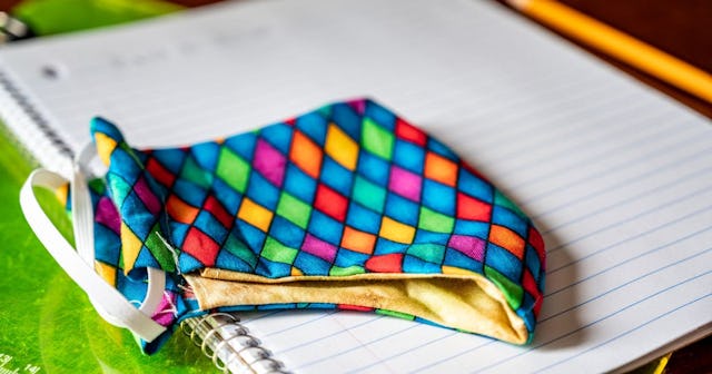 Face mask resting on top of back to school supplies of paper, pencil and a clip board