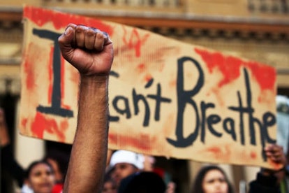 A man holds his fist in the air in front of a placard that reads 'I can't breathe'