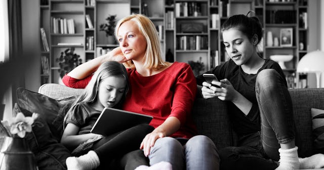 Sad mother sitting on couch with her daughters, playing with mobile devices