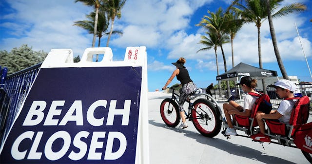 A cyclist with a trailer for children passes a "Beach Closed" sign on the boardwalk on March 22, 202...