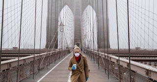 A woman wearing a mask walks the Brooklyn Bridge in the midst of the coronavirus outbreak on March 2...