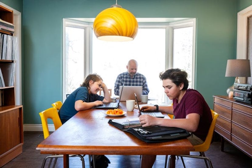 A woman working at her kitchen table. Her teen son is eating beside her.