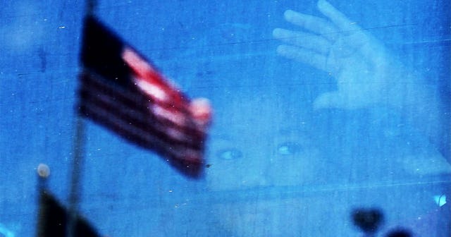 migrant child looks out the window of a bus as protesters try to block a bus carrying migrant childr...