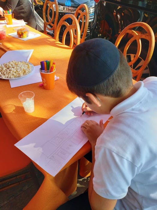 A child sitting at an orange table and drawing a picture in support of the #RebuildBreadberry moveme...