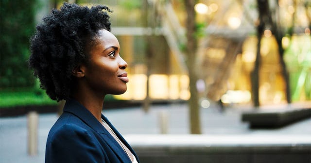 A woman in a blue blazer sitting next to a playground, smiling and looking off into the distance.