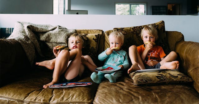 Siblings eating snacks watching TV while relaxing on sofa at home