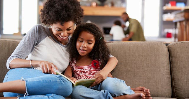 Mother And Daughter Sit On Sofa In Lounge Reading Book Together