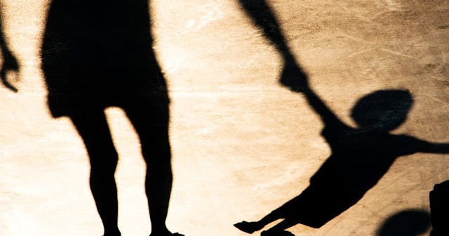 Shadows silhouettes of mother and son pulling her hand on summer promenade in sepia black and white