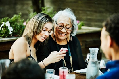 Granddaughter showing grandmother photos on smartphone during outdoor family dinner