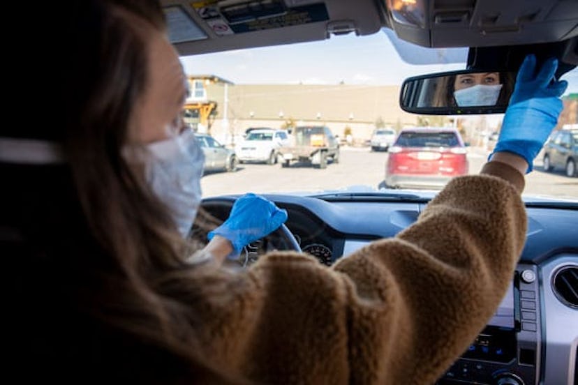 woman driving her vehicle wearing latex gloves and a mask during the COVID-19