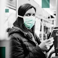 Young woman is driving in a bus and wearing a protection mask from virus and holding smart phone