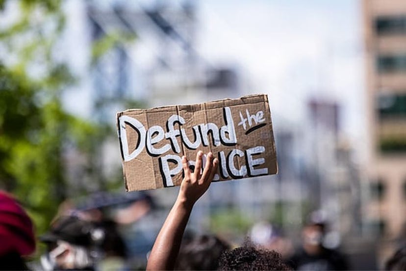 A protester holds up a homemade sign that says, "Defund the Police" with the Manhattan Bridge behind...