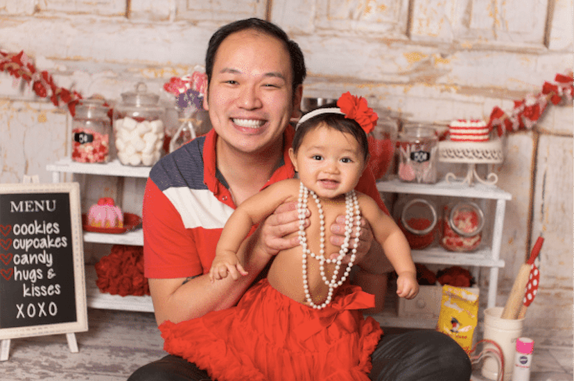 A man who became a single dad by surrogacy holding his little girl dressed in pearls and red flowers...