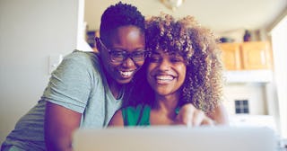 Laughing women hugging and using laptop