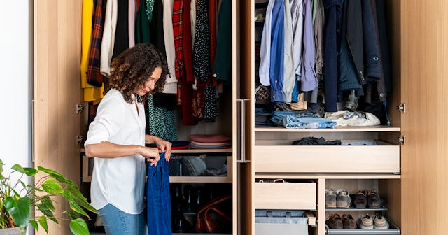 A young brown haired woman organizing a small wooden closet inside her home during a sunny day