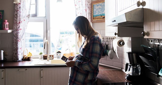 Blonde pregnant woman standing in the kitchen next to a window with an ultrasound picture of her soo...