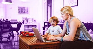 A mom chatting with her mom squad while using a laptop and her son looking at her laptop screen sitt...