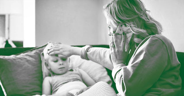 A mother in a sweatshirt talking on her smartphone while holding her hand on a girl's forehead who h...