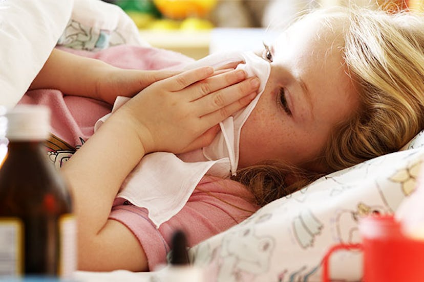 A blonde girl lying down with a sore throat, wiping her nose with a white cloth and medicine on the ...