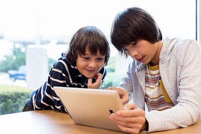 Older boy teaches younger boy to use digital tablet