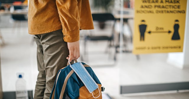 A college student holding a backpack and a face mask
