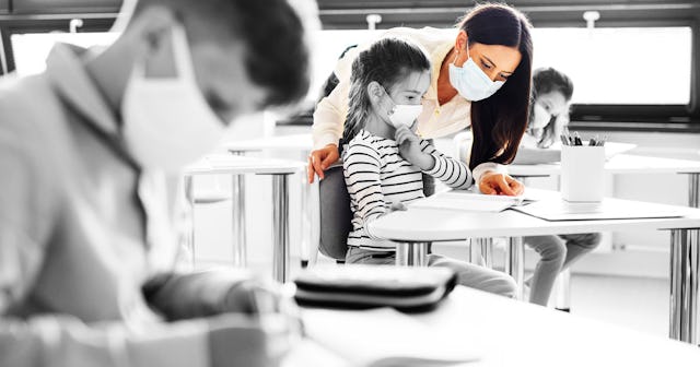 A teacher with a mask during a tough pandemic class in 2020 assisting a student