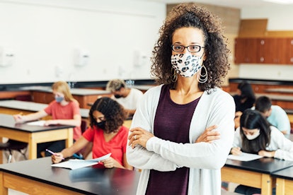 A teacher with a mask during a tough pandemic class in 2020 with students doing a test behind her ba...