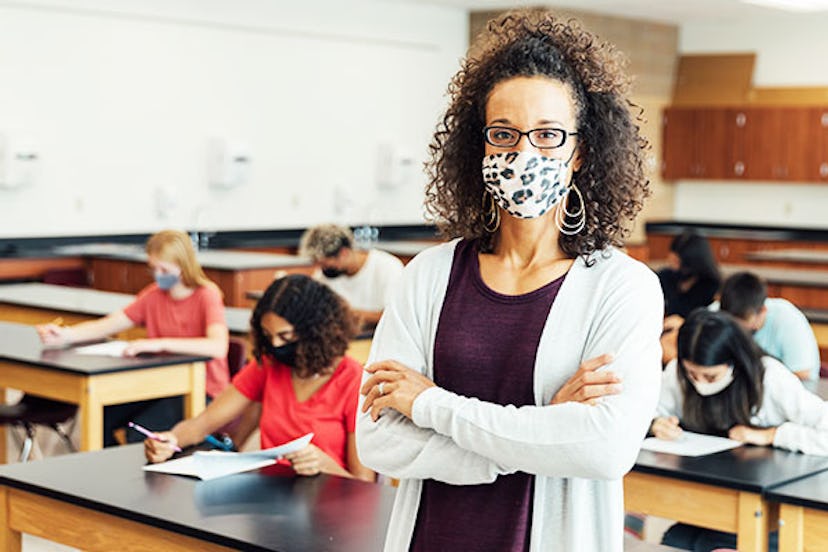 A teacher with a mask during a tough pandemic class in 2020 with students doing a test behind her ba...
