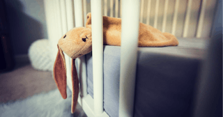 A brown plushie rabbit hanging out of a baby crib