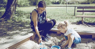 An older mom playing with her kid in a sandbox at a playground