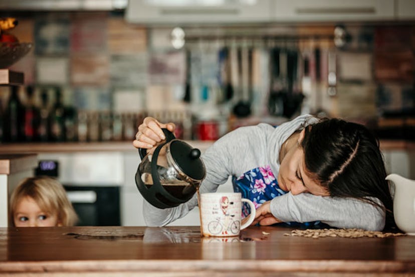 A woman leaning her head on a table, sipping coffee into a mug because she is tired and not a superm...