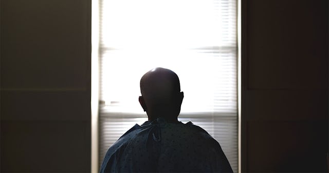 A COVID-19 patient sitting on a bed in the hospital and looking through a window in a dark room