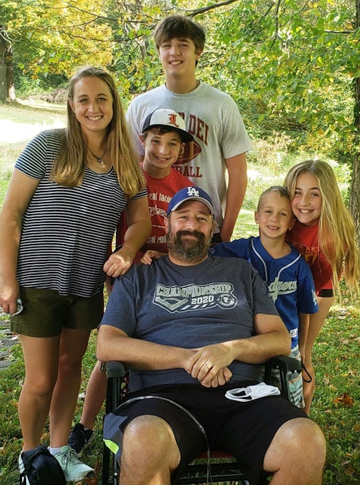 A man in a wheelchair surrounded by four children smiling and posing in a forest