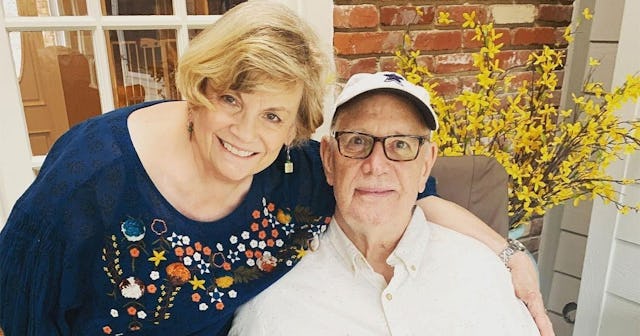 An elderly married couple smiling and posing at a terrace with their dog